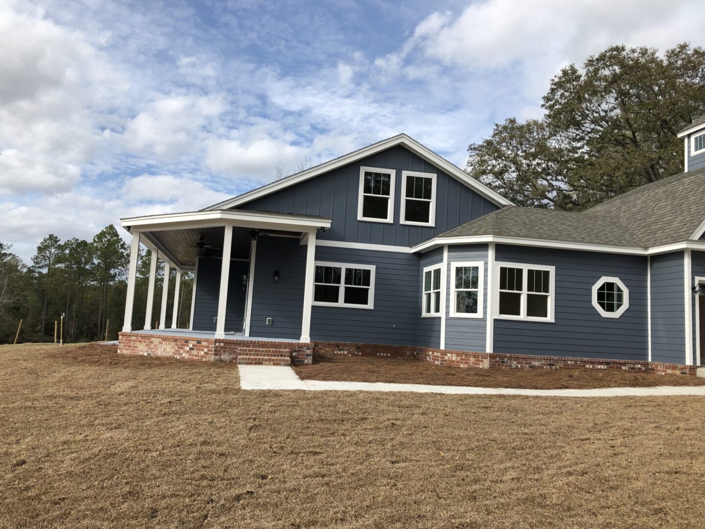 A blue house with a porch and a dirt field.